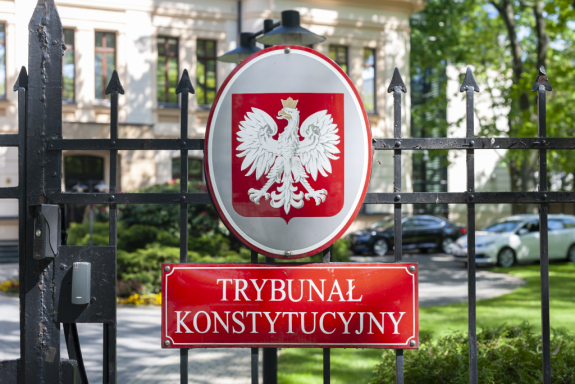 tablica na ogrodzeniu z napisem Trybunał Konstytucyjny z budynkiem w tle
