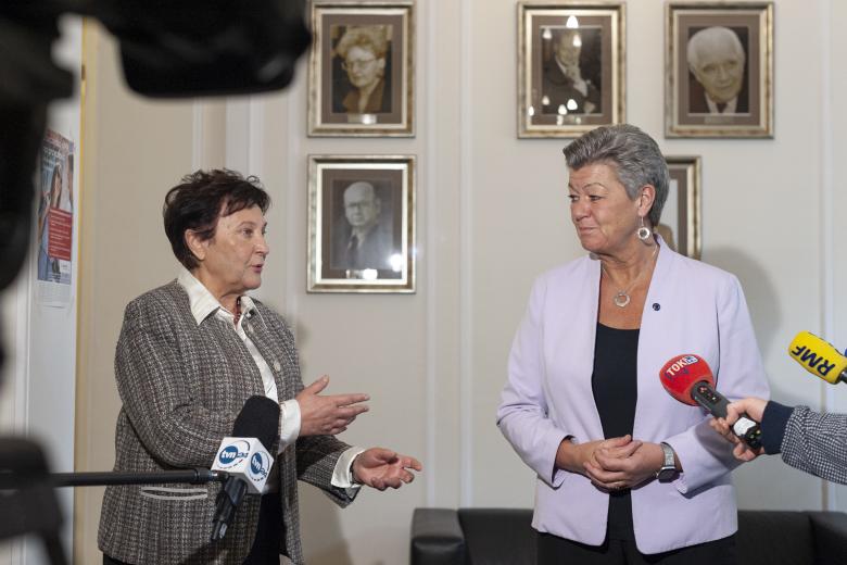 ZRPO Hanna Machińska i Komisarz Ylva Johansson wypowiadające się dla mediów na tle portretów przedstawiających byłych RPO