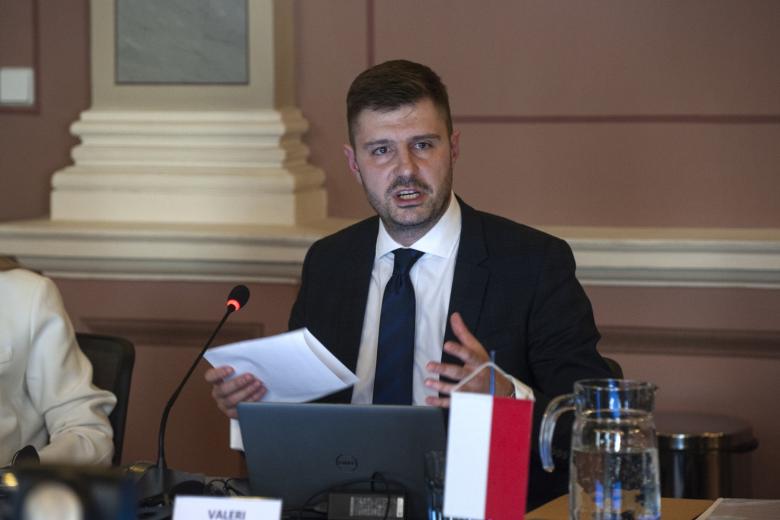ZRPO Valeri Vachev siedzi za stołem i przemawia, na stole na niewielkim stojaku polska flaga