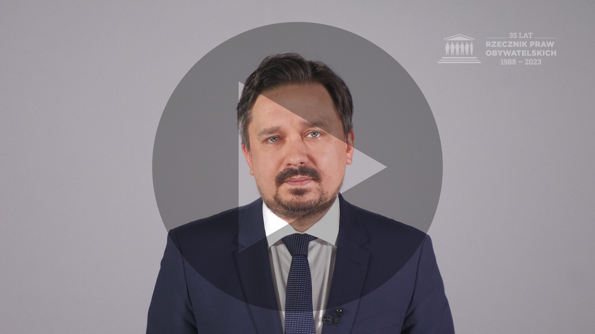 Kadr z nagrania przedstawiający RPO Marcina Wiącka z naniesionym symbolem odtwarzania wideo - trójkątem w kole