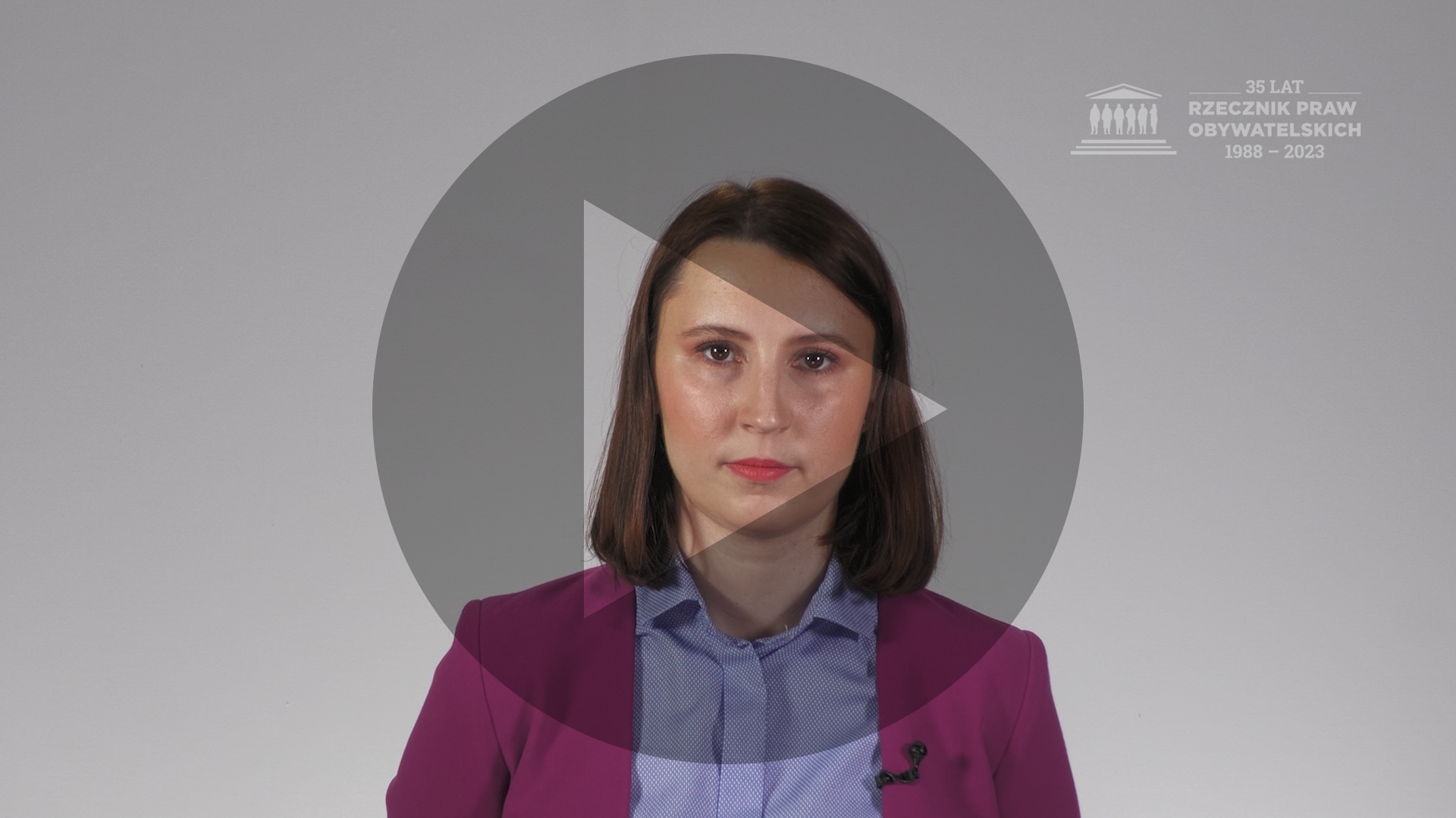Kadr nagrania przedstawiający Monikę Wiszyńską-Rakowską. Na kadr naniesiony jest symbol odtwarzania - trójkąt w kole