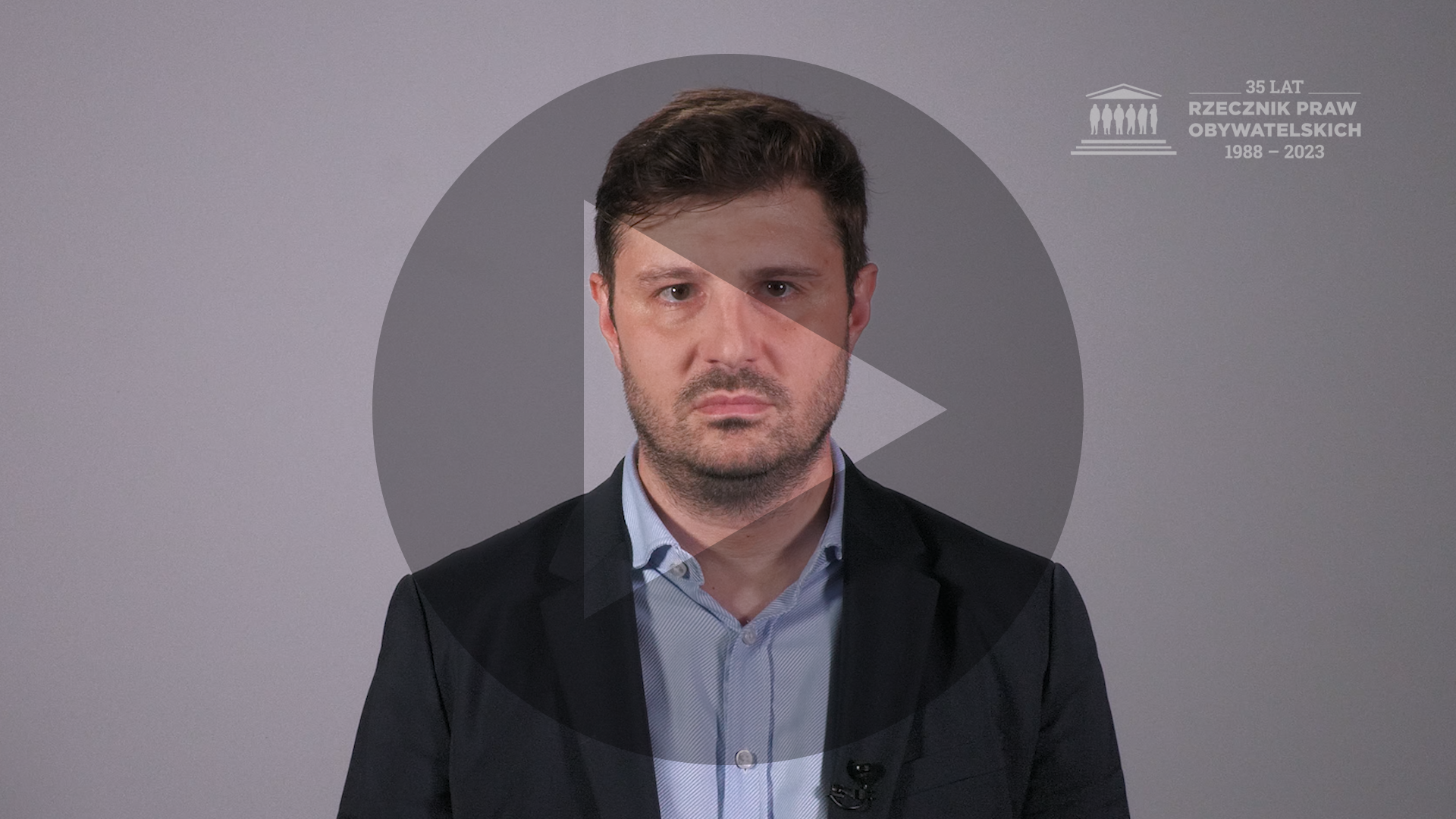 Kadr z nagrania przedstawiający RPO Marcina Wiącka i tłumaczkę polskiego języka migowego z naniesionym symbolem odtwarzania wideo - trójkątem w kole