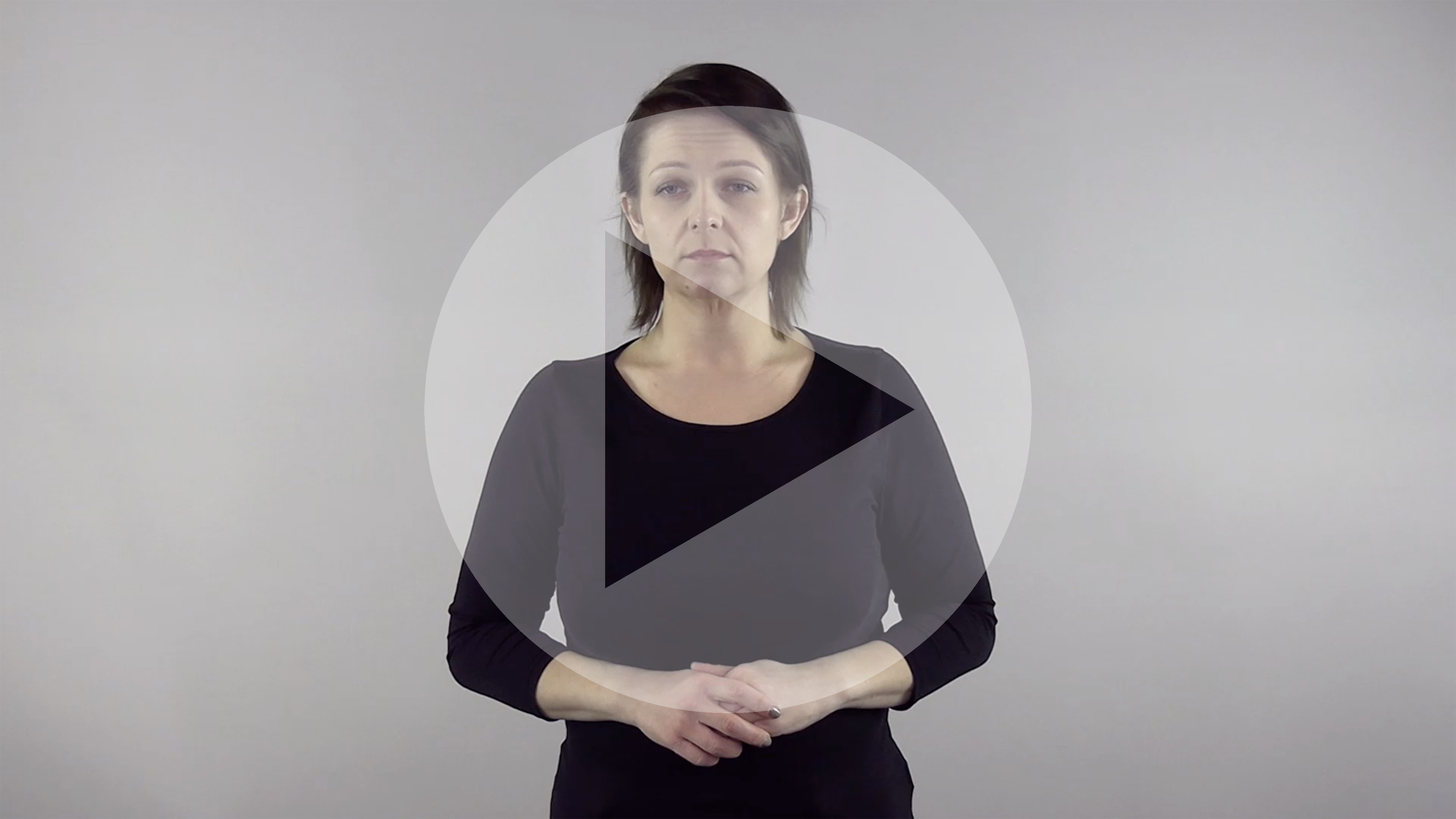 Kadr z nagrania przedstawiający kobietę porozumiewającą się w Polskim Języku Migowym z naniesionym symbolem odtwarzania wideo - trójkątem w kole