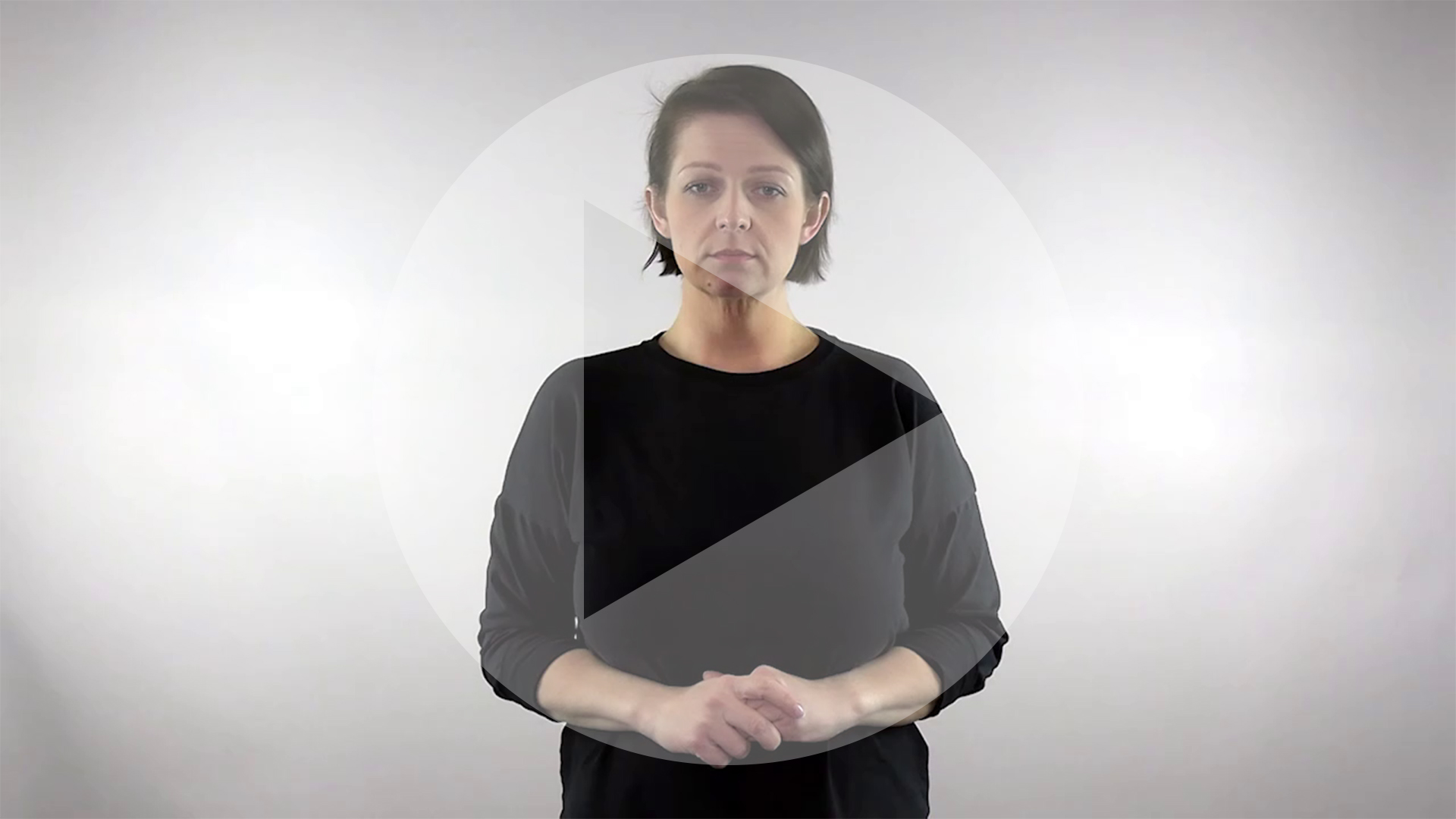 Kadr z nagrania przedstawiający tłumaczkę języka migowego z naniesionym symbolem odtwarzania wideo - trójkątem w kole