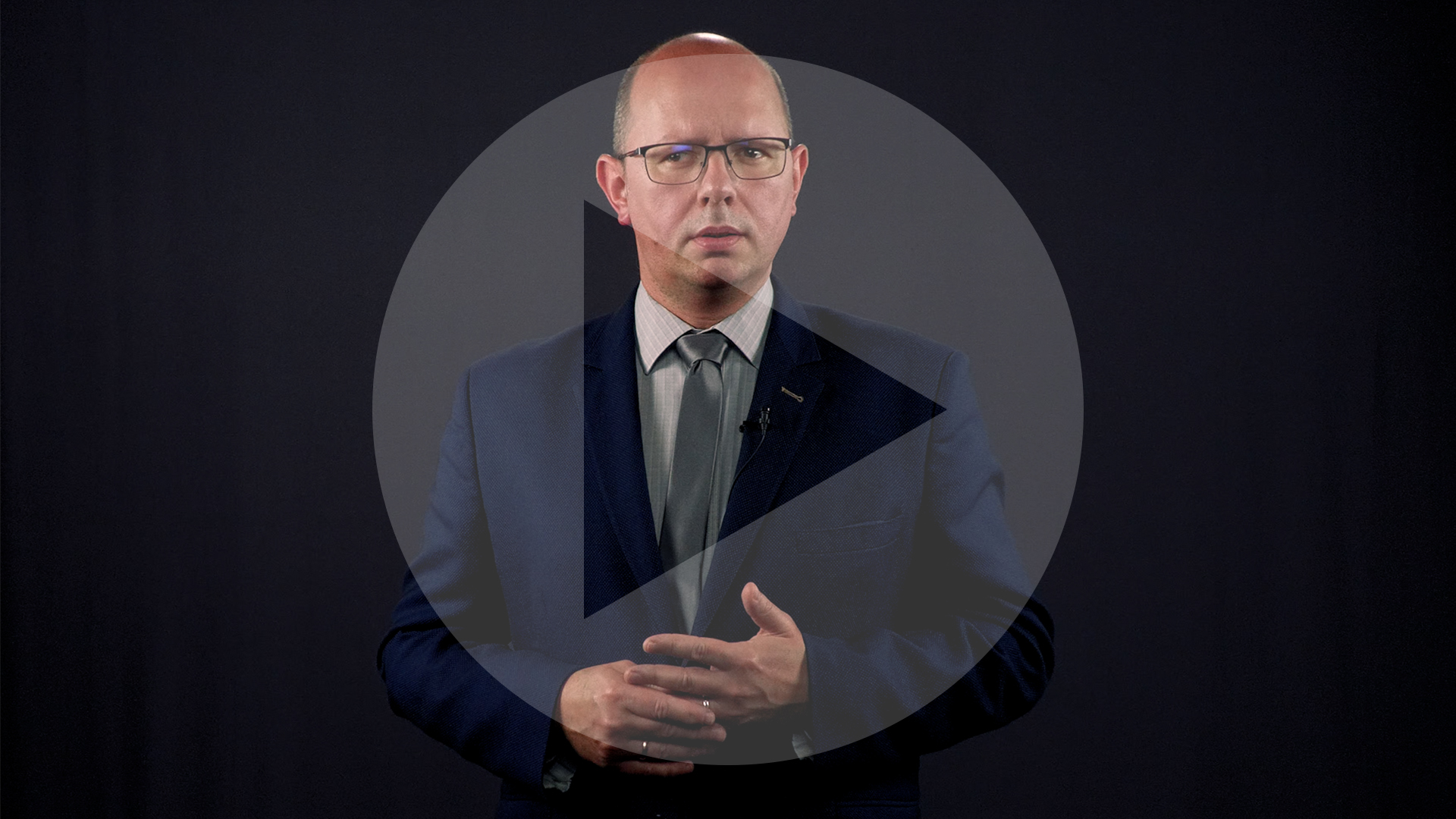 Kadr z nagrania przedstawiający Błażeja Kmieciaka. Na kadr naniesiony jest symbol odtwarzania wideo - trójkąt w kole