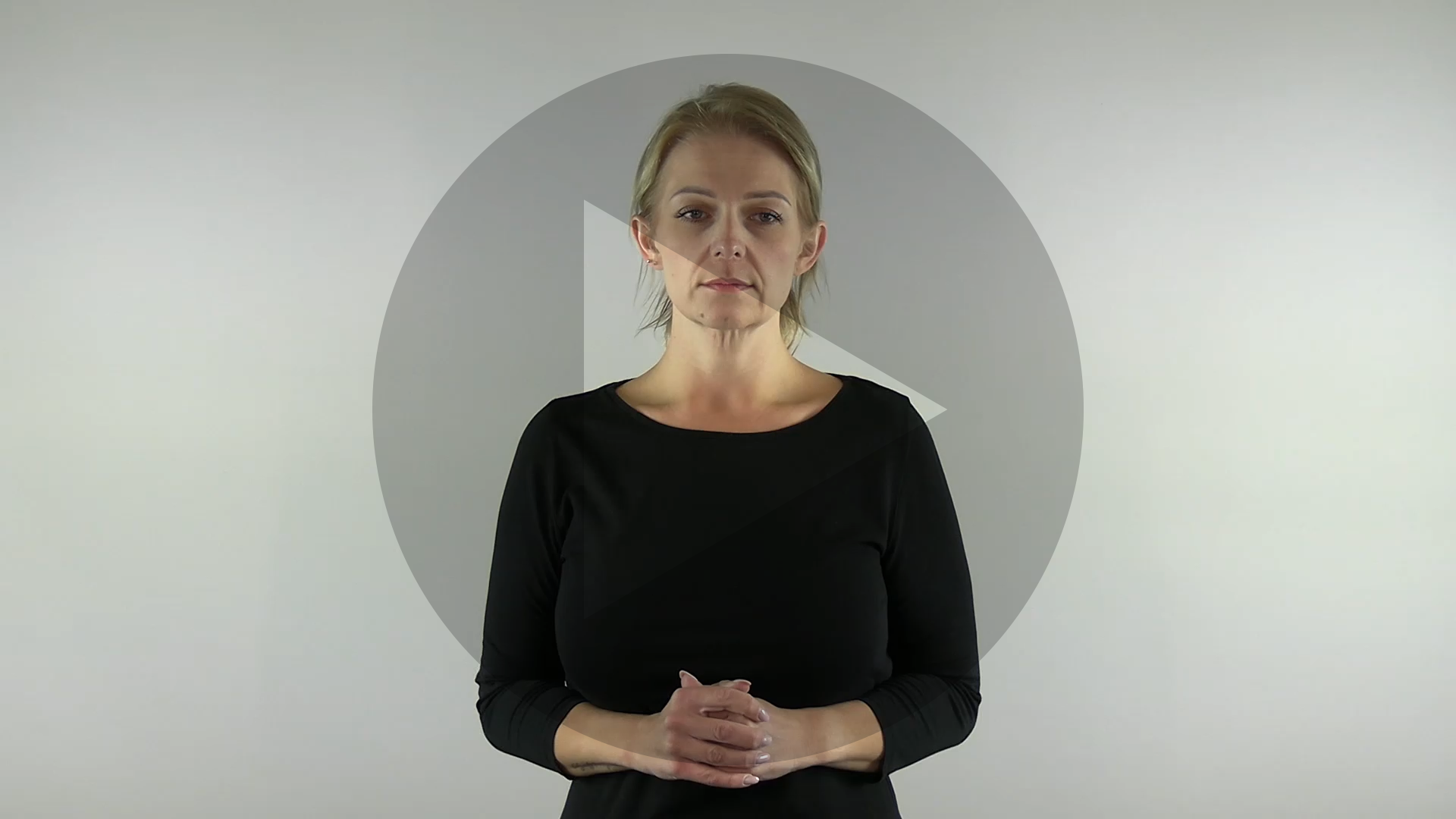 Kadr nagrania przedstawiający sylwetkę tłumaczki języka migowego. Na kadr jest naniesiony znak odtwarzania wideo - trójkąt w kole