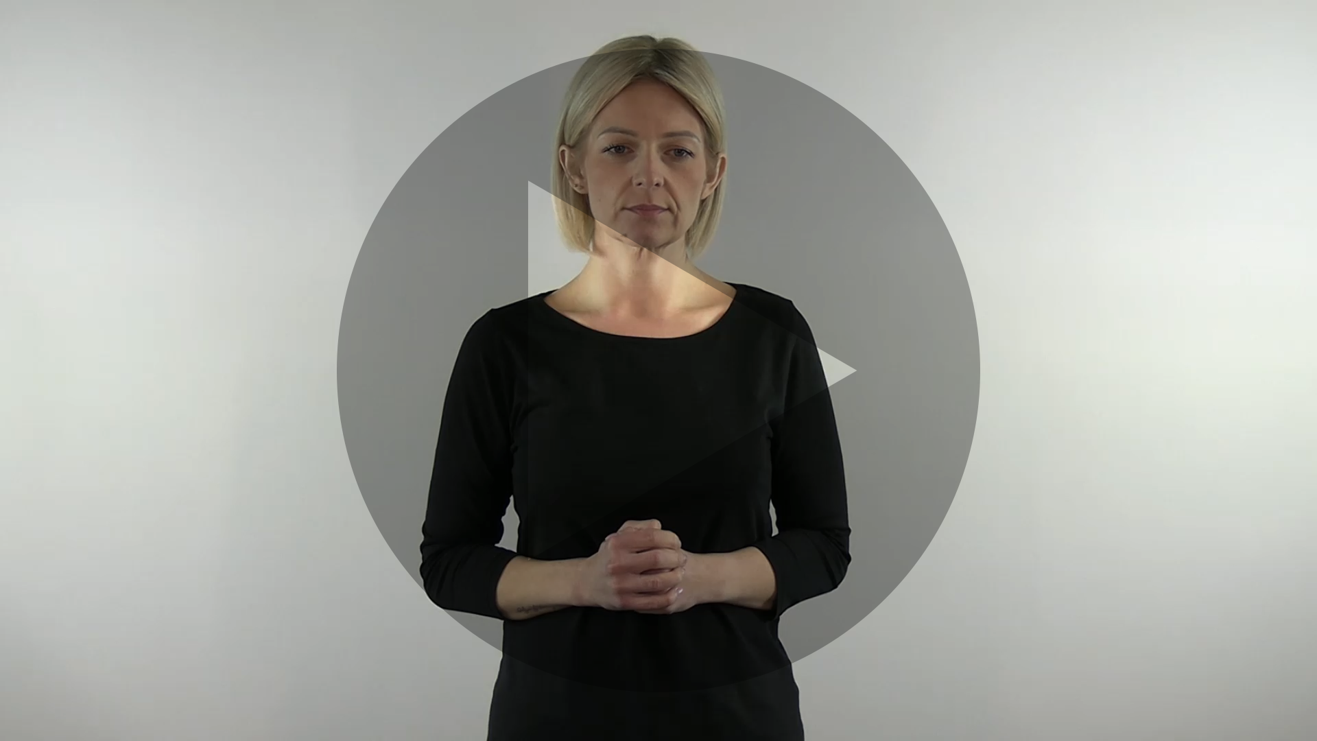 Kadr nagrania przedstawiający sylwetkę tłumaczki języka migowego. Na kadr jest naniesiony znak odtwarzania wideo - trójkąt w kole