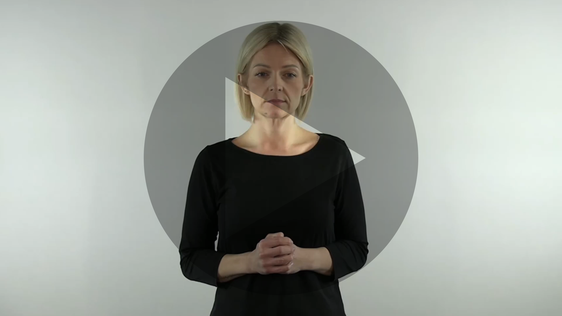 Kadr nagrania przedstawiający sylwetkę tłumaczki języka migowego. Na kadr jest naniesiony znak odtwarzania wideo - trójkąt w kole