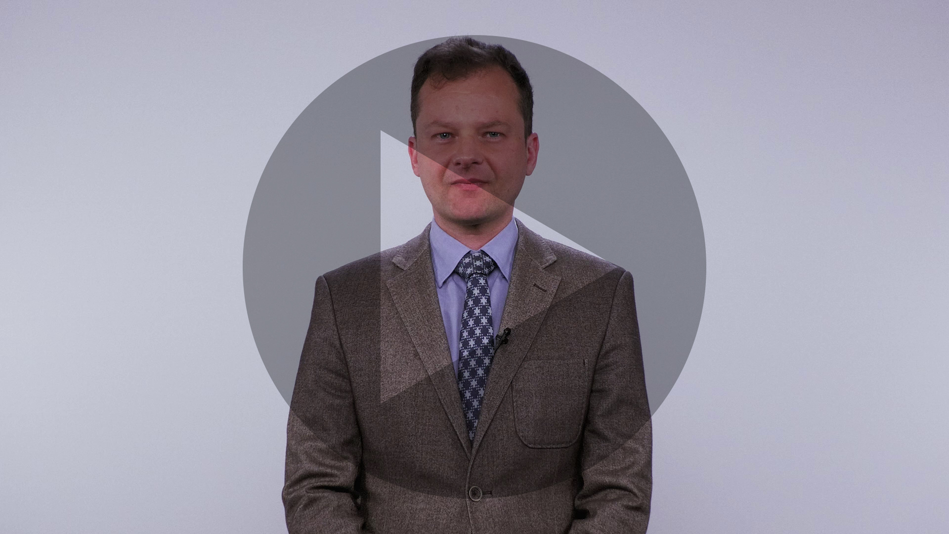 kadr z nagrania z widocznym mówiącym mężczyzną i nałożonym trójkątnym symbolem odtrwarzania wideo