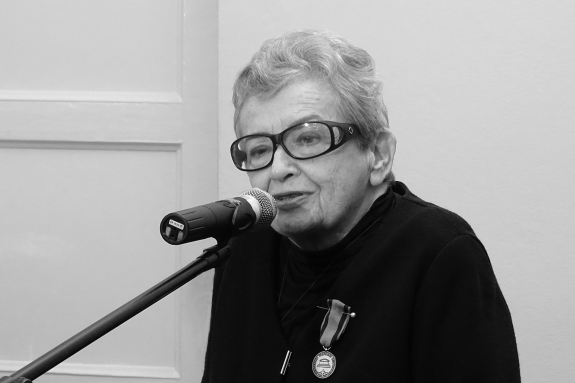 Czarno-białe zdjęcie Haliny Bortnowskiej wypowiadającej się do mikrofonu. Do jej piersi przypięta jest odznaka honorowa RPO "Za Zasługi dla Ochrony Praw Człowieka"