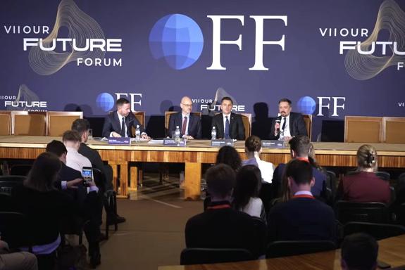 Cztery osoby siedzą za stołem w sali konferencyjnej, przysłuchuje się im kilkadziesiąt osób siedzących na sali