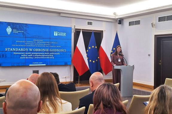 osoba przemawia w sali na stojąco