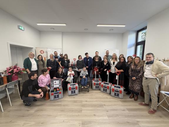 Zdjęcie grupowe ok. 20 osób stojących w pomieszczeniu. Przed nimi stoi 5 skrzyneczek pomocy sensorycznej