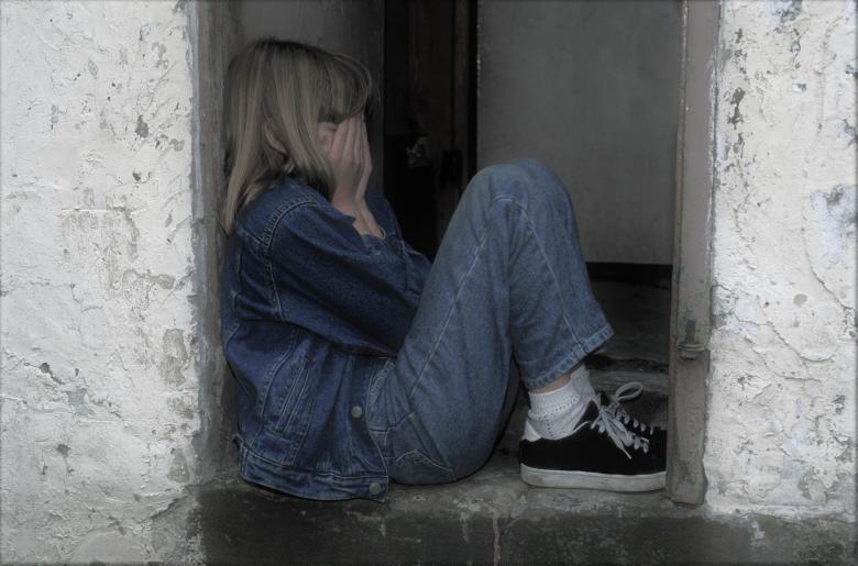 Skulona zrozpaczona dziewczyna siedzi w wejściu do domu