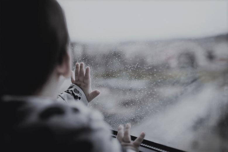 zdjęcie dziecka patrzącego przez szybę na padający deszcz 