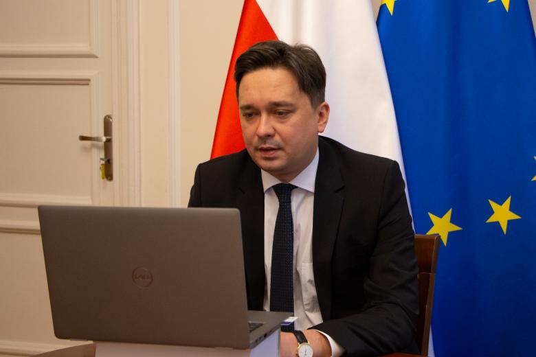 Mężczyzna siedzi przed komputerem, w tle flaga Polski i Unii Europejskiej