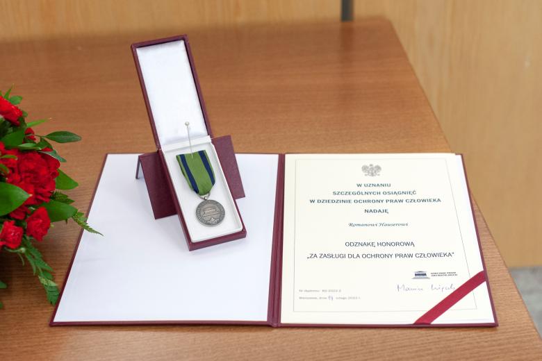 Zdjęcie odznaki RPO i dyplomu o treści "W uznaniu szczególnych osiągnięć w dziedzinie ochrony praw człowieka, nadaję Romanowi Hauserowi odznakę honorową "za zasługi dla ochrony praw człowieka""