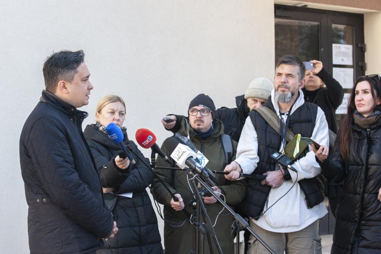 RPO Marcin Wiącek wypowiadający się dla mediów przed budynkiem szkoły w Hajnówce. Słucha go grupa dziennikarzy trzymających mikrofony.