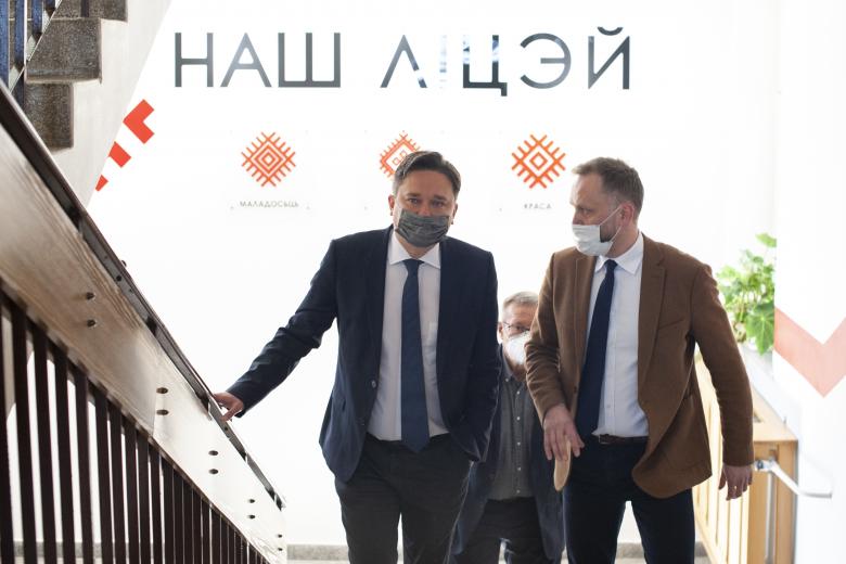 RPO Marcin Wiącek oraz dyrektor Liceum wchodzą po szkolnych schodach. W tle jest ściana z białoruskimi symbolami ludowymi oraz tekstem w języku białoruskim.