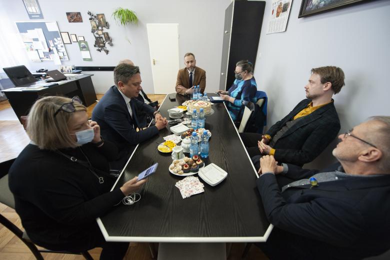 RPO Marcin Wiącek, pracownicy Biura RPO oraz dyrektor liceum rozmawiają przy stole. Na stole znajduje się poczęstunek i marcinek - tradycyjne podlaskie ciasto.
