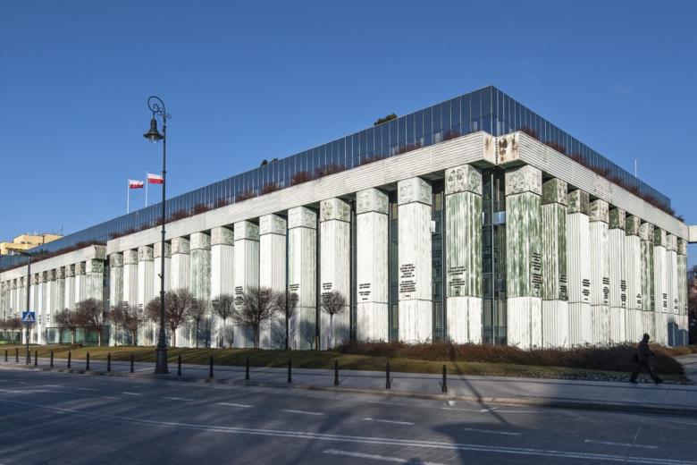 nowoczesny, szklany budynek otoczony zieloną kolumnadą