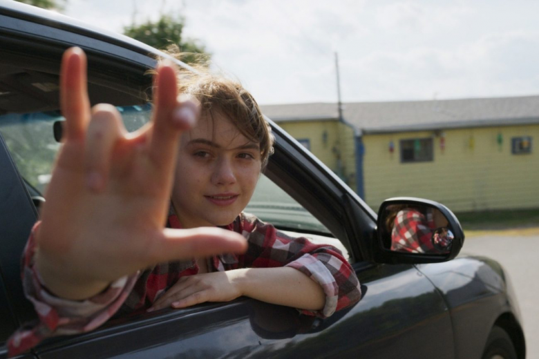 Kadr z filmu "CODA" przedstawiający uśmiechniętą główną bohaterkę wychylającą się z okna samochodu i wykonującą gest w języku migowym