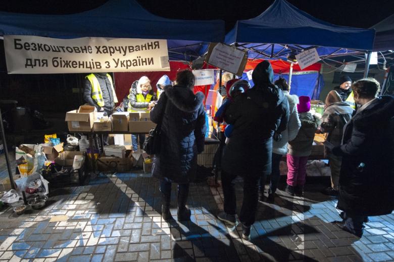 Grupa osób przed namiotem z pomocą humanitarną. Na namiocie napisy w języku ukraińskim
