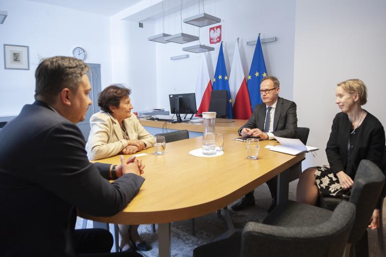 RPO Marcin Wiącek, Hanna Machińska oraz dwuosobowa delegacja z ambasady Finlandii rozmawiają przy stole konferencyjnym. W tle godło Polski i flagi Polski i Unii Europejskiej