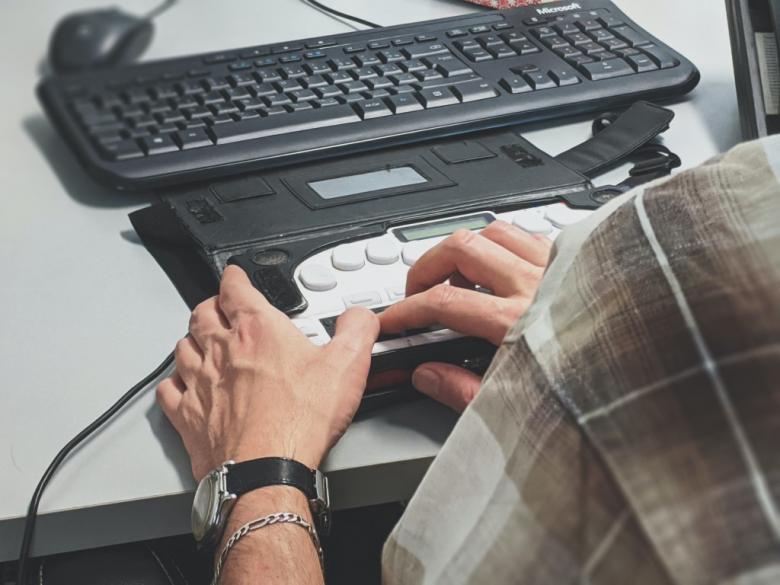 Zdjęcie komputera z nakładką dla osób niedowidzących z dłoniami człowieka na klawiaturze