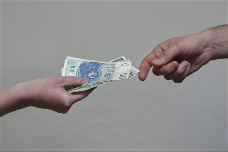 zdjęcie dłoni osoby podającej plik pieniędzy 