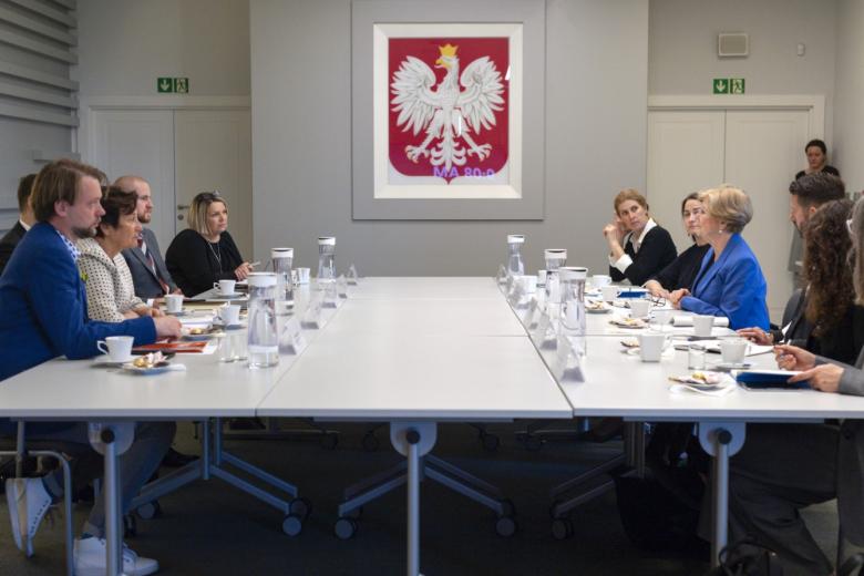 Grupa kilkunastu osób siedząca przy stole konferencyjnym, w tle godło Polski