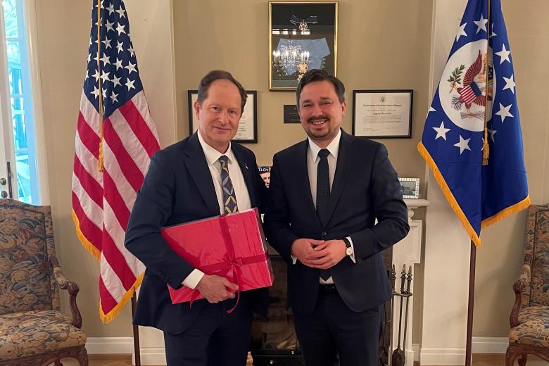 RPO Marcin Wiącek i ambasador USA Mark Brzeziński pozujący w gabinecie ambasadora na tle flag USA