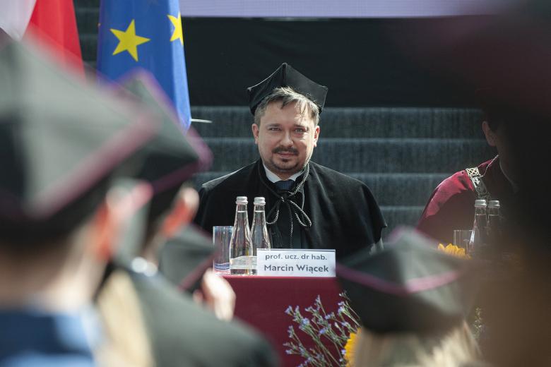 RPO Marcin Wiącek siedzi w todze uniwersyteckiej za stołem na zakończeniu roku akademickiego na WPiA UW