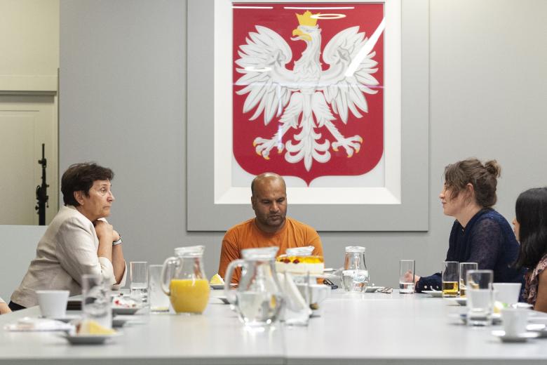 Cztery osoby siedzące przy stole, w tle godło Polski