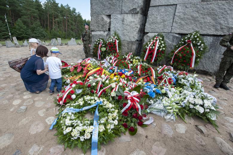 Matka z dwójką małych dzieci oglądają wieńce złożone pod pomnikiem. Przy pomniku pełni wartę dwóch żołnierzy