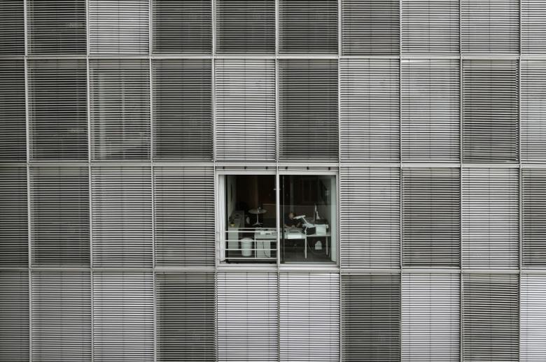 zdjęcie budynku biurowego z jednym odsłoniętym oknem, gdzie ktoś pracuje