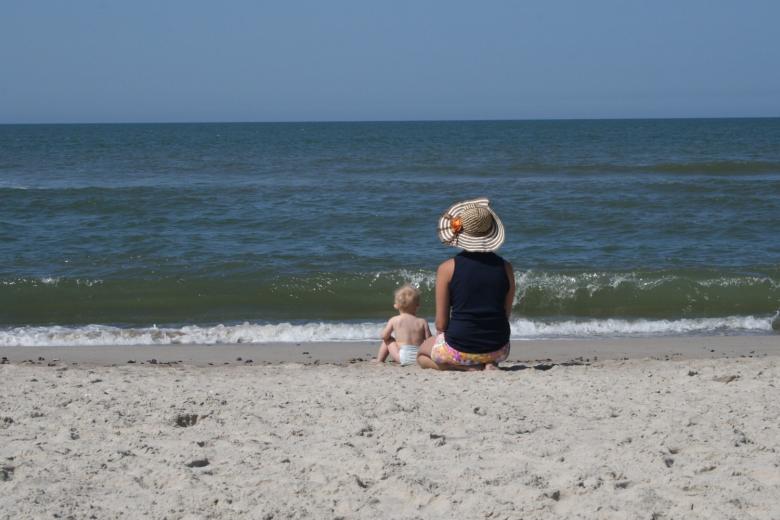 Małe dziecko bawiące się z opiekunem na morskiej plaży w słoneczny dzień