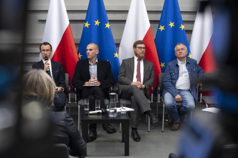 Cztery osoby siedzą na tle flag Polski i UE