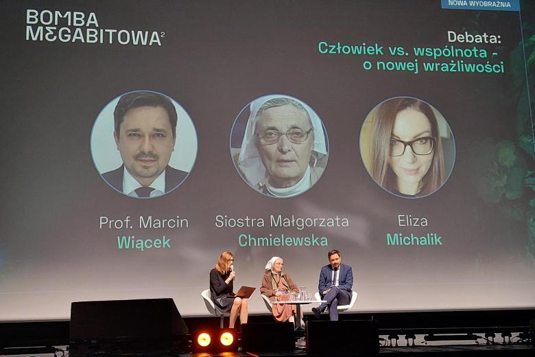 Trzy osoby siedzą na fotelach na dużej scenie, w tle wyświetlona duża grafika z portretami i napisem: Bomba Megabitowa, Prof. Marcin Wiącek, Siostra Małgorzata Chmielewska, Eliza Michalik
