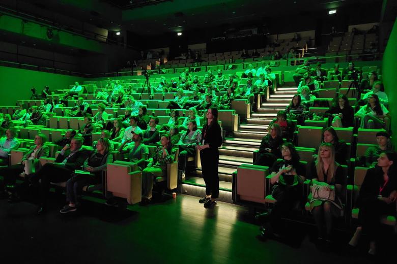 Kilkadziesiąt osób siedzi na widowni w dużej sali kina lub teatru