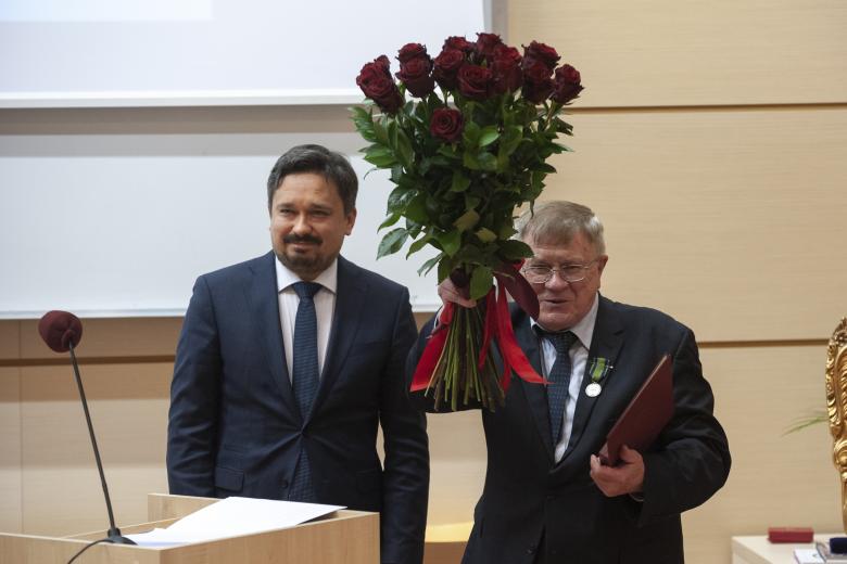 RPO Marcin Wiącek i prof. Grzybowski stoją obok siebie. Marcin Wiącek uśmiecha się, a prof. Grzybowski z przypiętą w klapę marynarki odznaką unosi bukiet kwiatów w górę