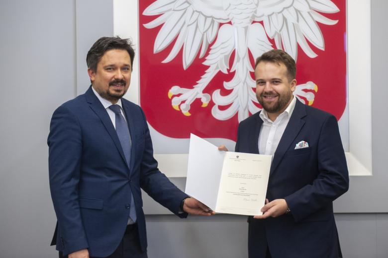 RPO Marcin Wiącek i prezydent Starachowic Marek Materka pozują do zdjęcia na tle godła Polski trzymając akt powołania