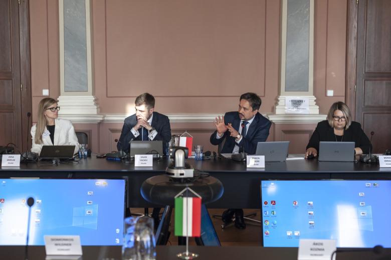 Cztery osoby siedzą za stołem, na którym stoi niewielka polska flaga