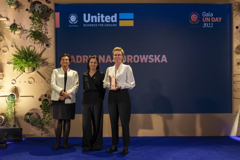 Trzy kobiety pozują do zdjęcia stojąc na tle planszy z napisem "Adrianna Porowska". Jedna z nich trzyma w dłoniach statuetkę