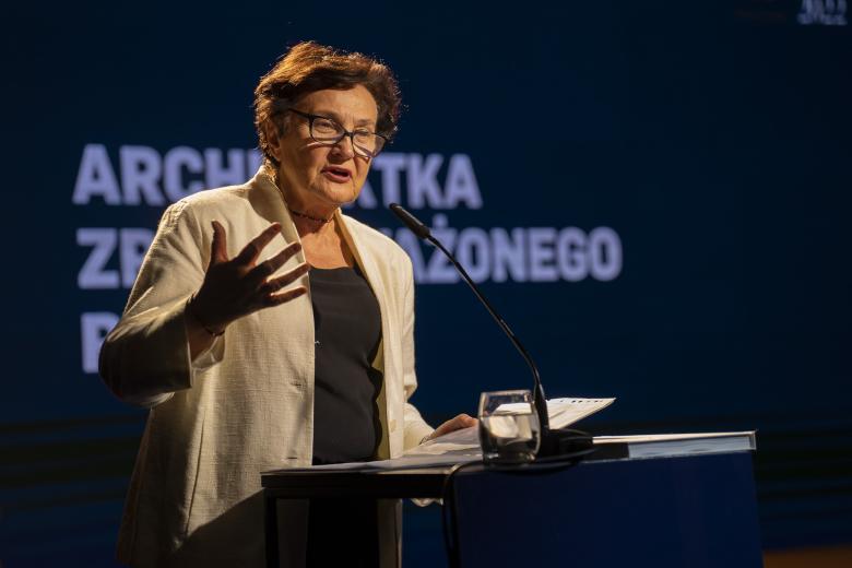 ZRPO Hanna Machińska stoi za mównicą i wygłasza przemówienie, w tle wyświetlacz z napisem "Architekta Zrównoważonego Rozwoju"