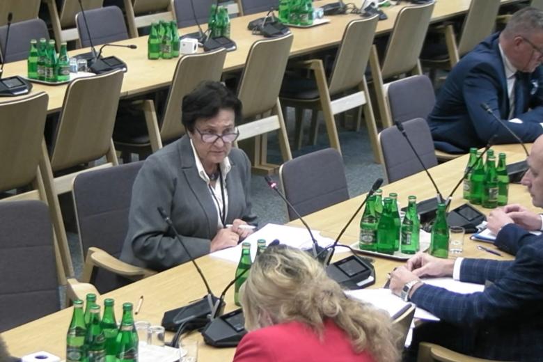 ZRPO Hanna Machińska siedzi za stołem i mówi do mikrofonu, na stole rozłożone dokumenty, przy stole siedzą inne osoby
