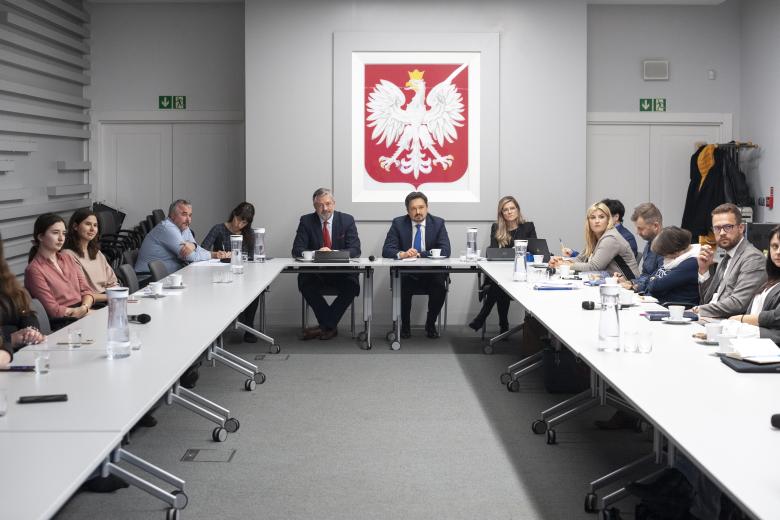 RPO Marcin Wiącek i pracownicy biura rozmawiają z goścmi przy dużym stole konferencyjnym. W tle godło Polski