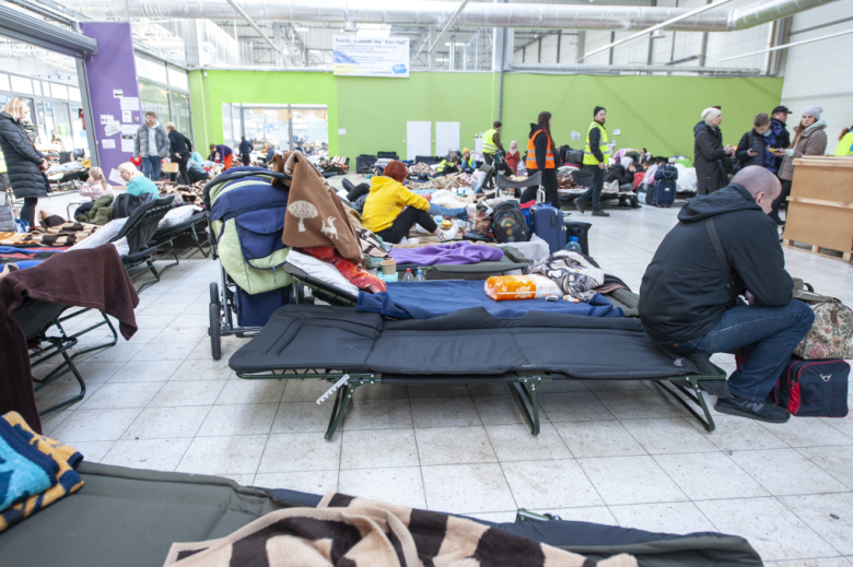 migranci siedzą na łóżkach polowych w punkcie recepcyjnym