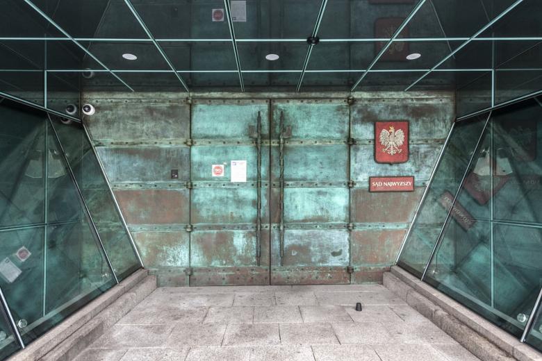 Ciężkie, dwuskrzydłowe drzwi w zielonkawym odcieniu, obok godło Polski i tabliczka z napisem "Sąd Najwyższy"