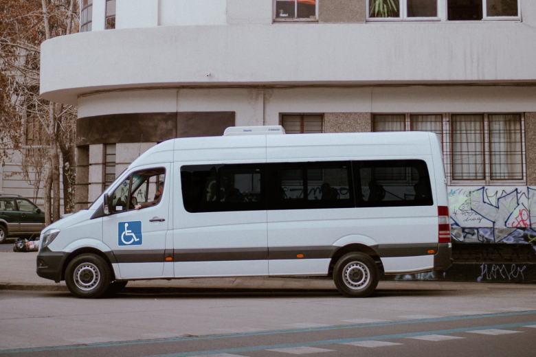 Biała furgonetka z symbolem niepełnosprawności - osoby poruszającej się na wózku - zaparkowana wzdłuż ulicy